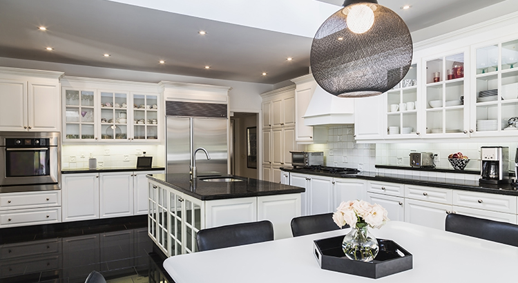 White breakfast table with black leather chairs, white wood and glass pane island with black granite countertop, cupboards in country style kitchen, black granite tile flooring